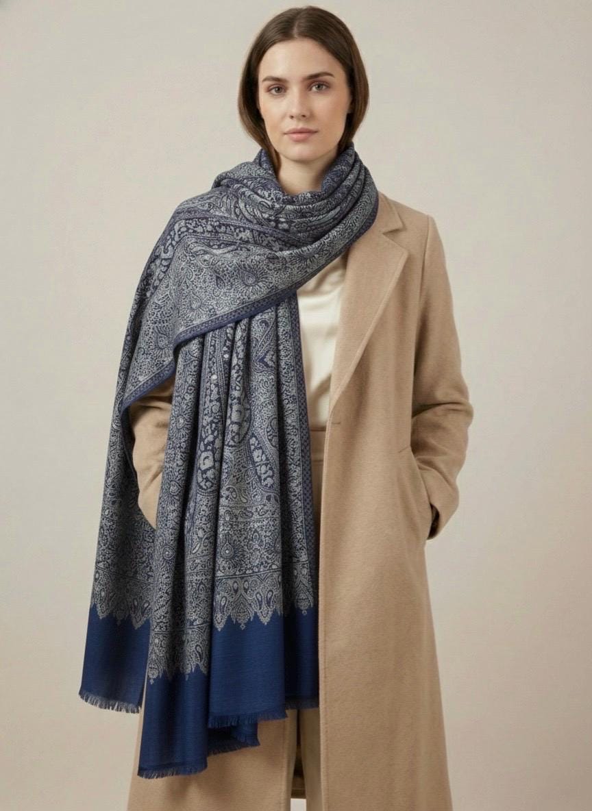 Woman wearing a blue patterned scarf and beige coat on a plain background