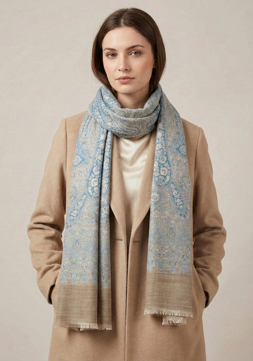 Woman wearing a patterned scarf and beige coat against a neutral background