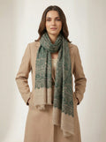 Woman wearing a beige coat and green patterned scarf on a plain background