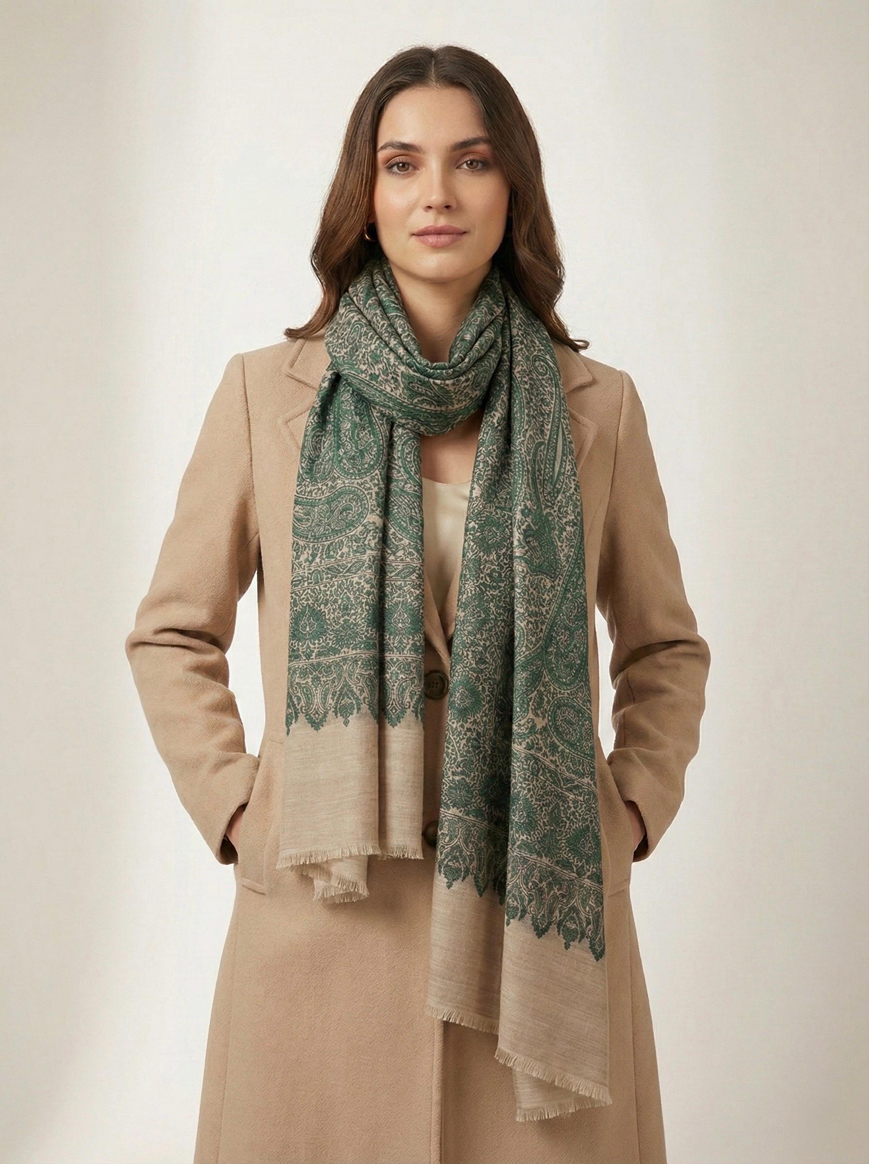 Woman wearing a beige coat and green patterned scarf on a plain background