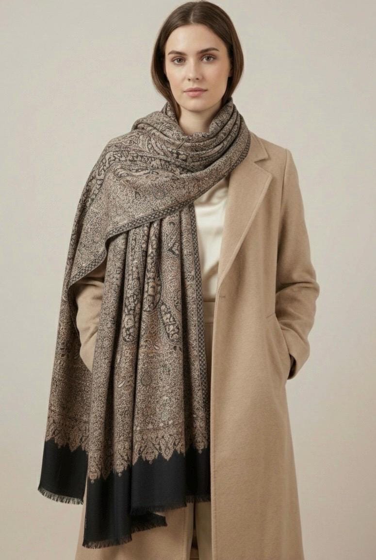 Woman wearing a patterned scarf and beige coat against a plain background