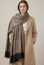 Woman wearing a patterned scarf and beige coat against a plain background