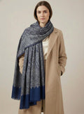 Woman wearing a blue patterned scarf and beige coat on a plain background