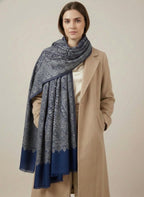 Woman wearing a blue patterned scarf and beige coat on a plain background
