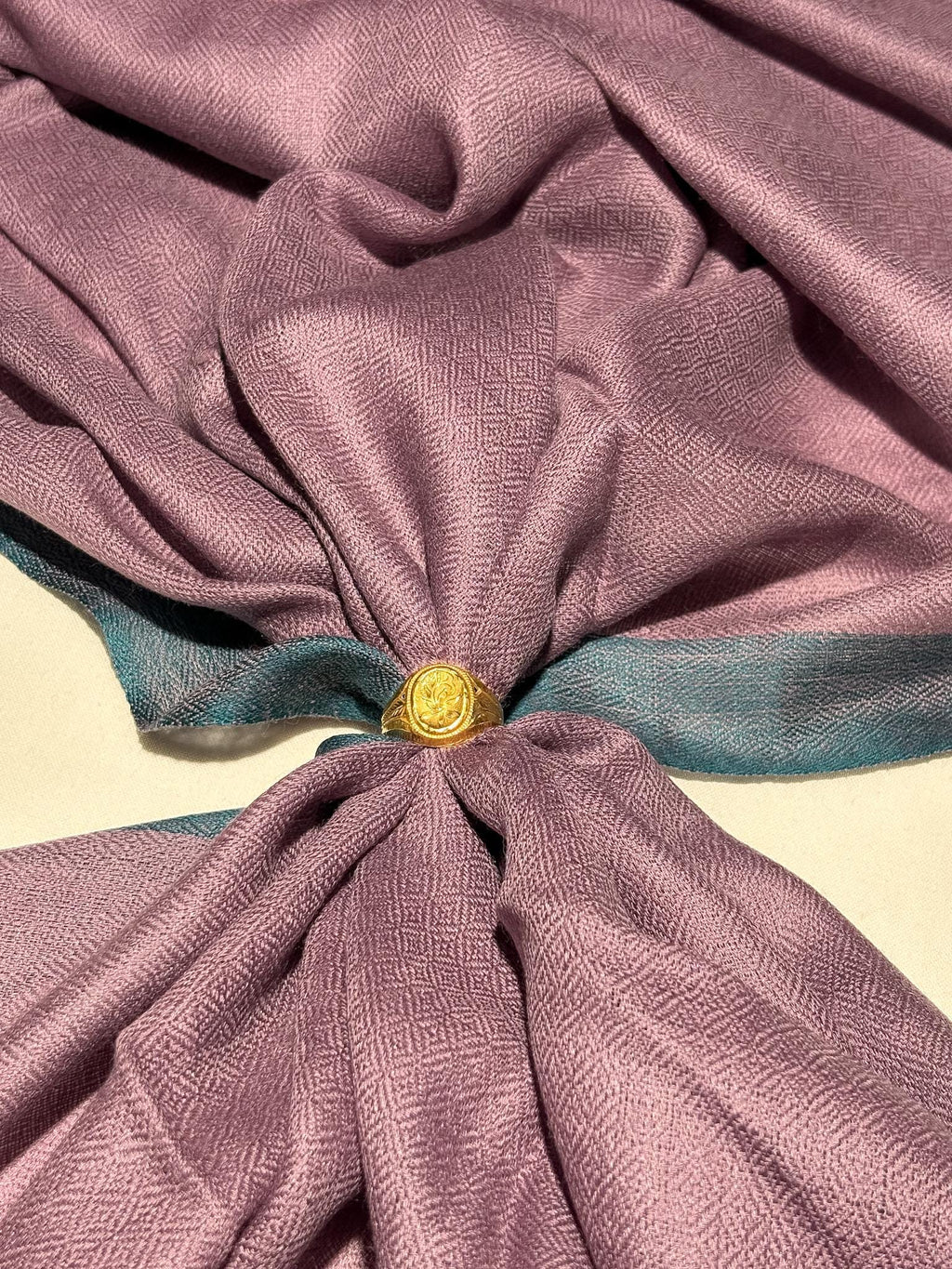 Close-up of a knotted fabric with a gold ring in the center on a beige background