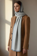 Woman wearing a light gray hijab and brown coat against a neutral background