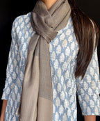 Person wearing a patterned shirt and brown scarf against a dark background