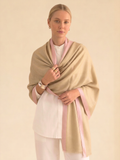 Woman wearing a beige shawl with pink trim over a white outfit on a beige background