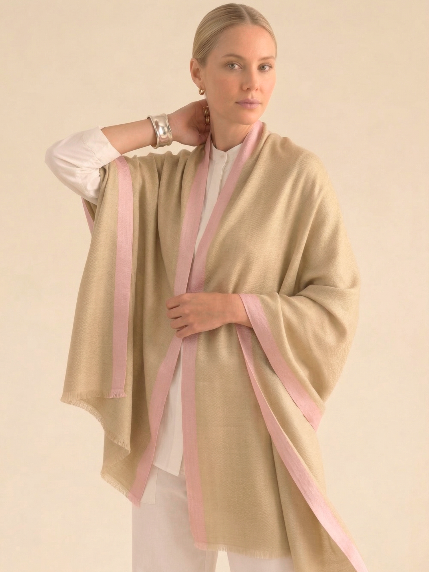 Woman wearing a beige shawl with pink stripes on a plain background