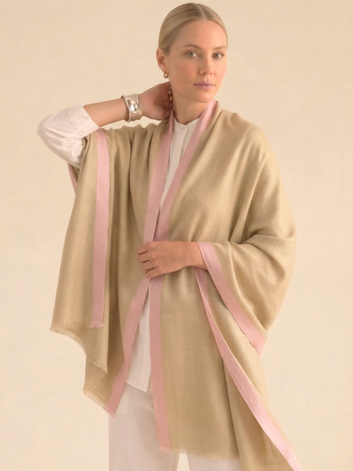 Woman wearing a beige shawl with pink stripes on a plain background