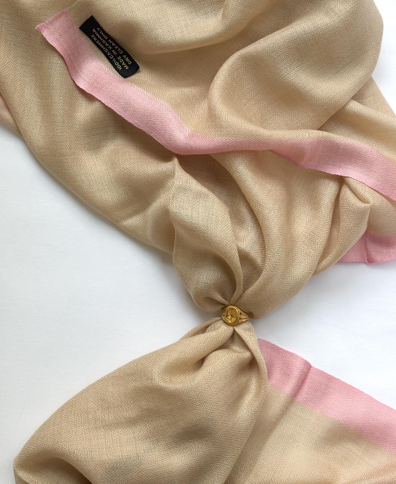 Beige scarf with pink trim tied into a knot on a white background
