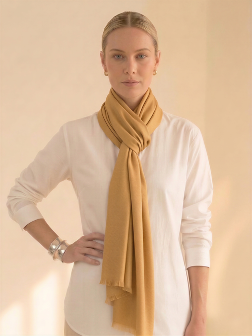 Woman wearing a mustard yellow scarf around her neck against a beige background