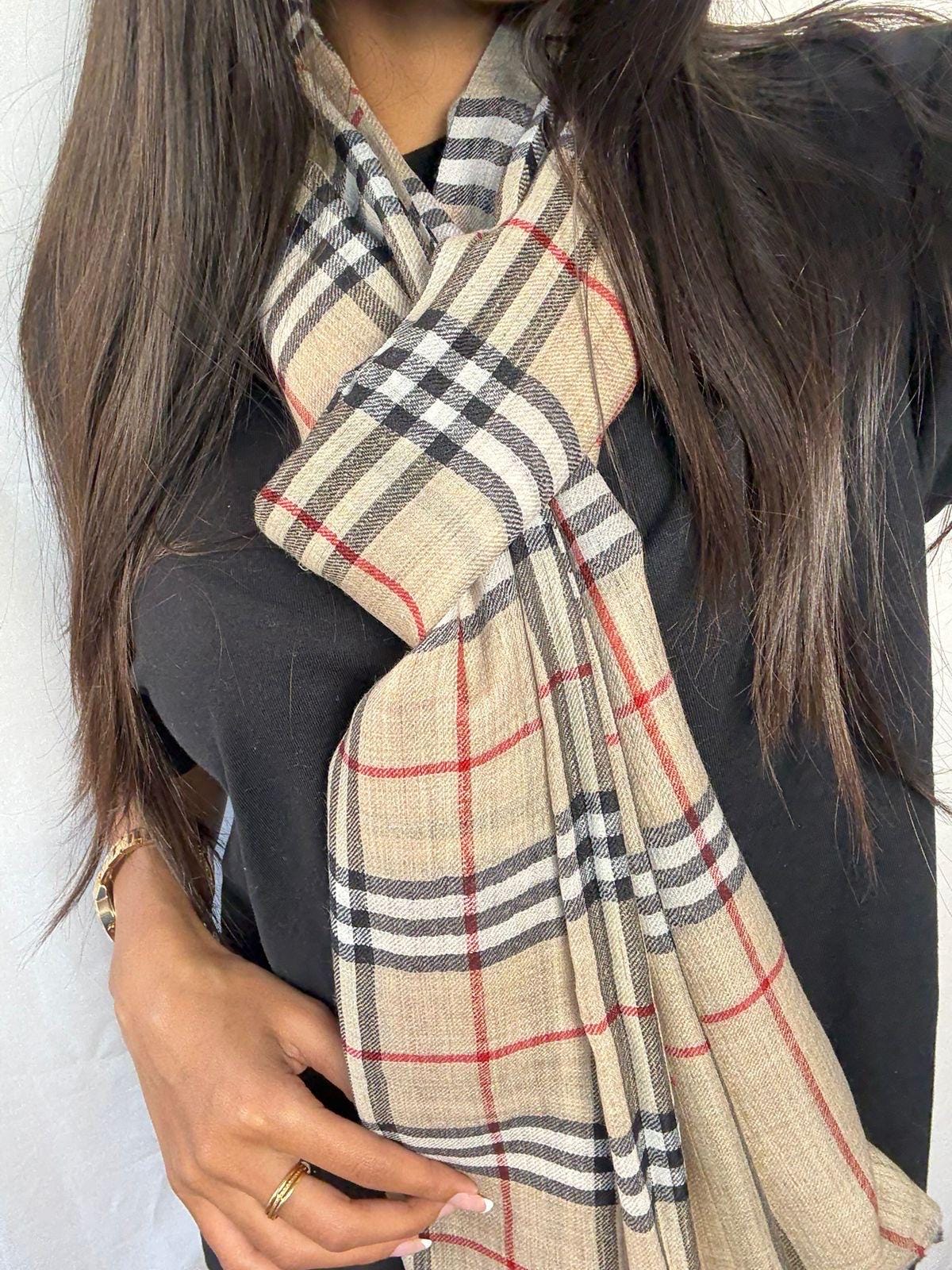 Person wearing a beige checkered scarf with a plain background