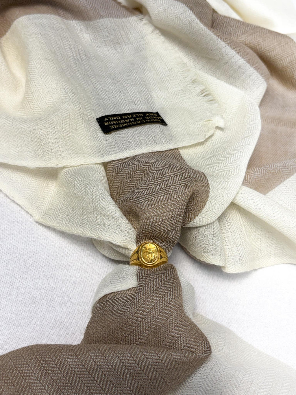 Close-up of a beige and brown scarf with a gold button and visible brand label.