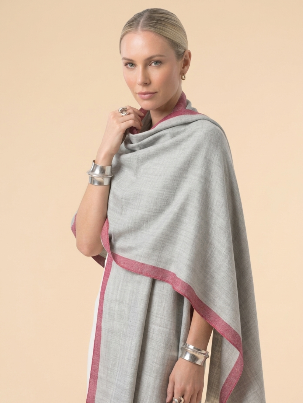 Woman wearing a gray poncho with pink trim against a beige background