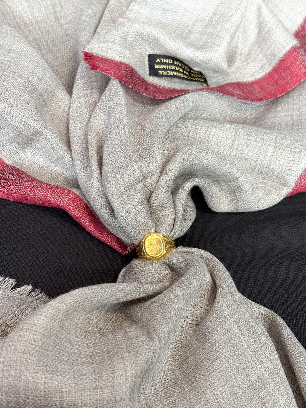 Close-up of a gray fabric with red trim and a gold button, featuring a brand label.