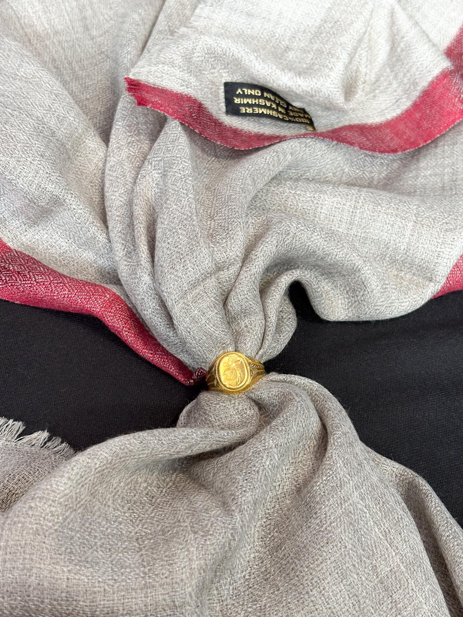Close-up of a gray fabric with red trim and a gold button, featuring a brand label.