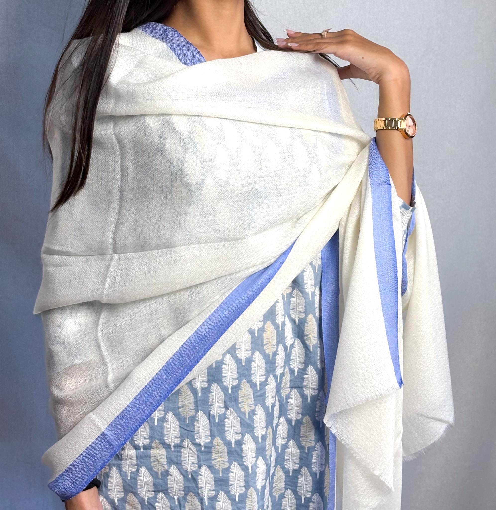 Woman wearing a white saree with blue patterns on a plain background