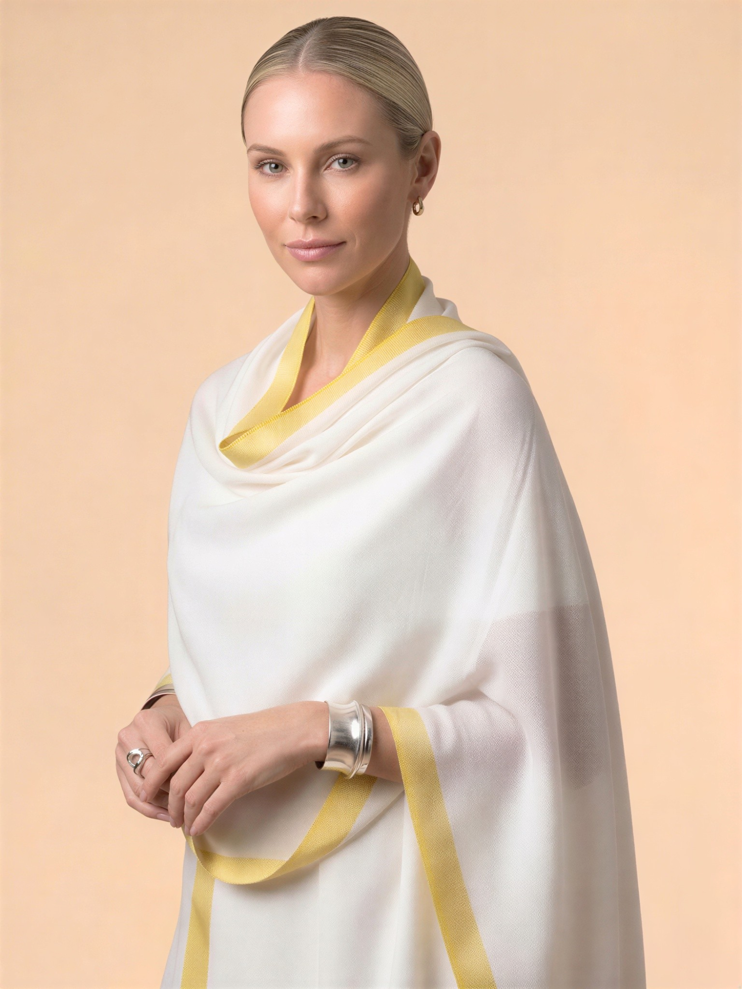 Woman wearing a white shawl with yellow trim on a beige background