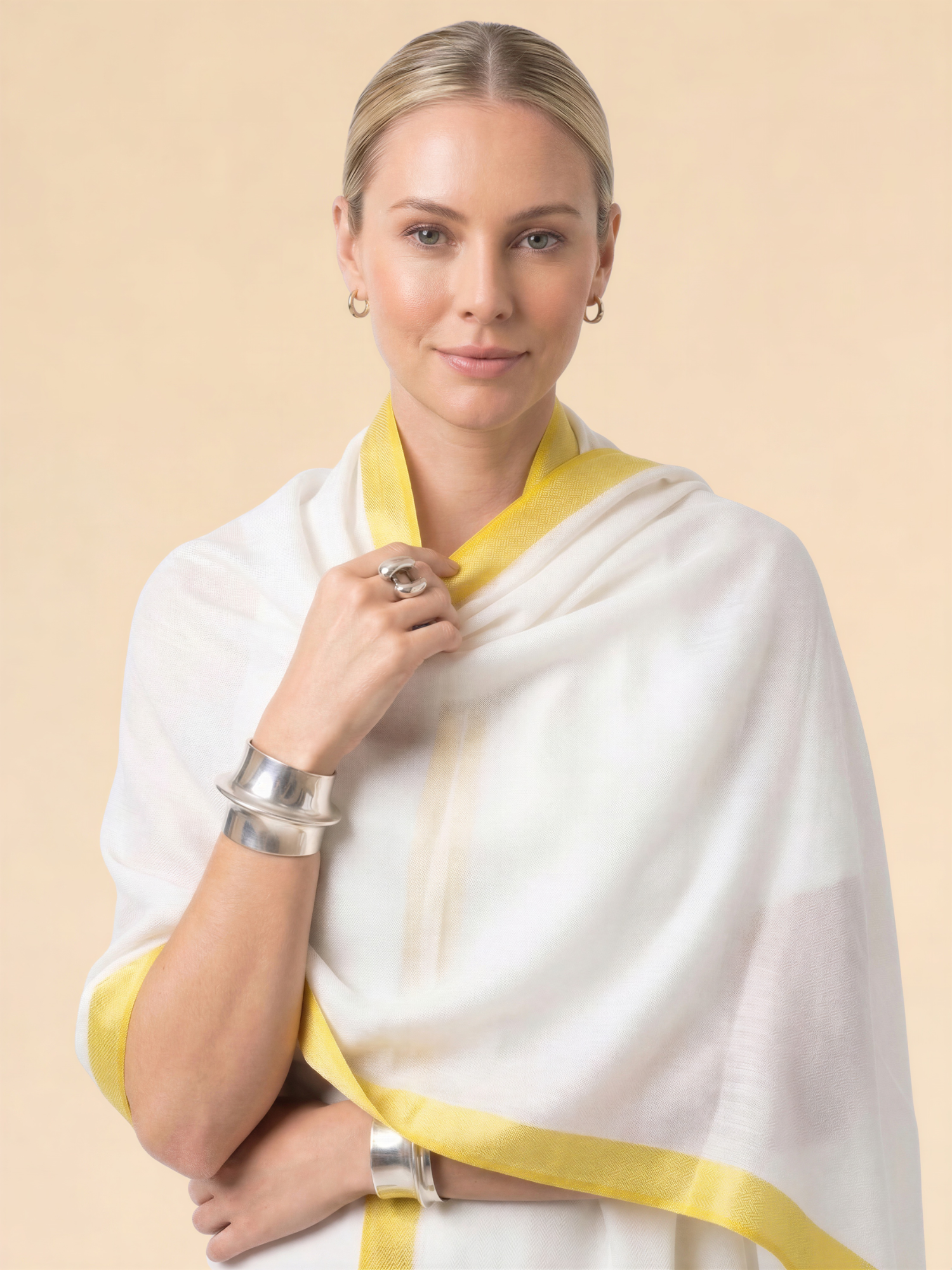 Woman wearing a white saree with yellow border on a beige background