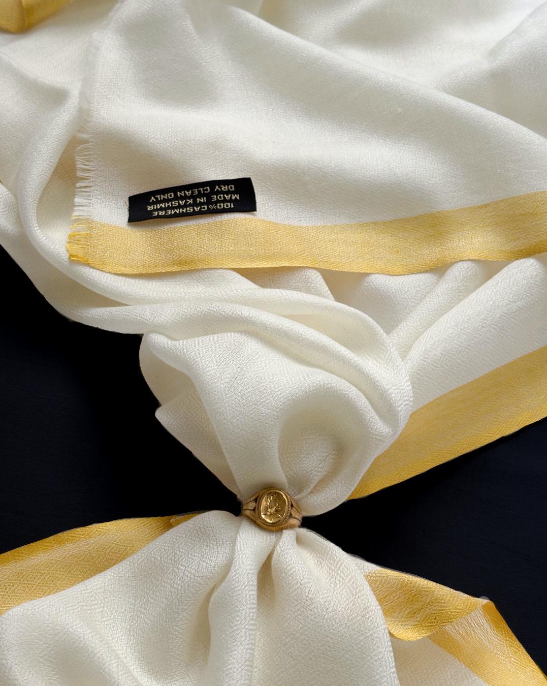 Close-up of a white garment with gold trim and a visible label on a black background