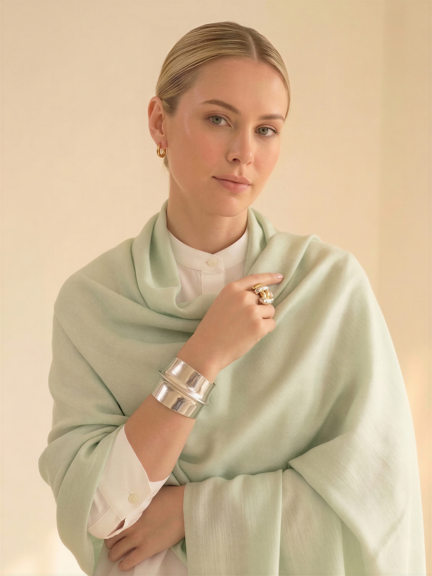 Woman wearing a light green scarf and silver jewelry against a beige background