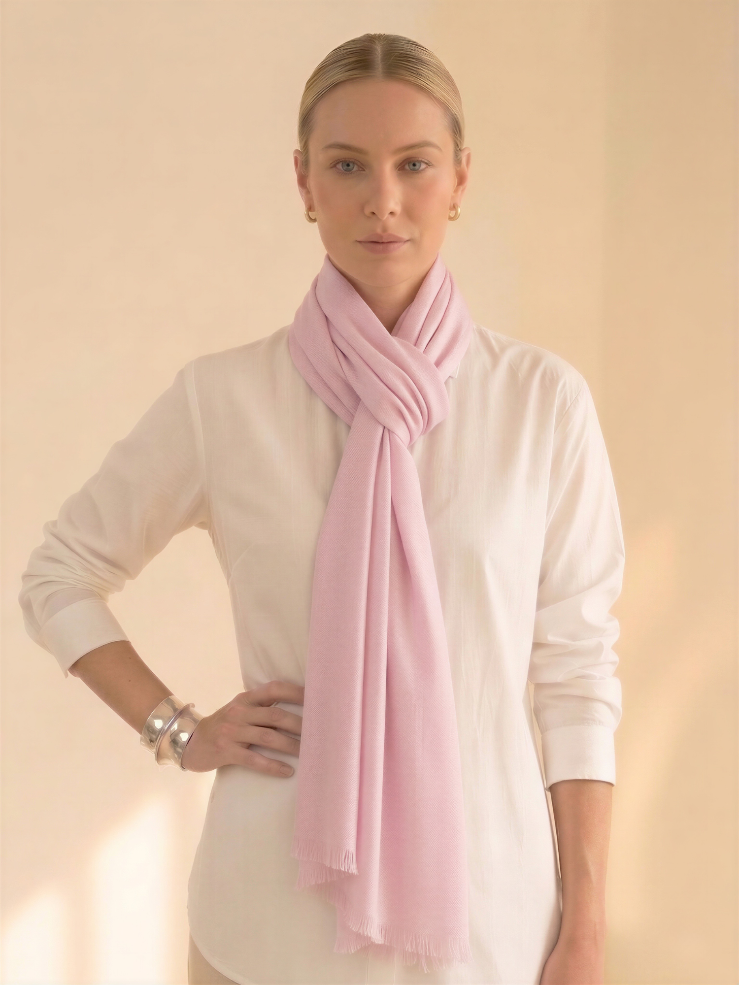 Woman wearing a light pink scarf and white shirt against a beige background