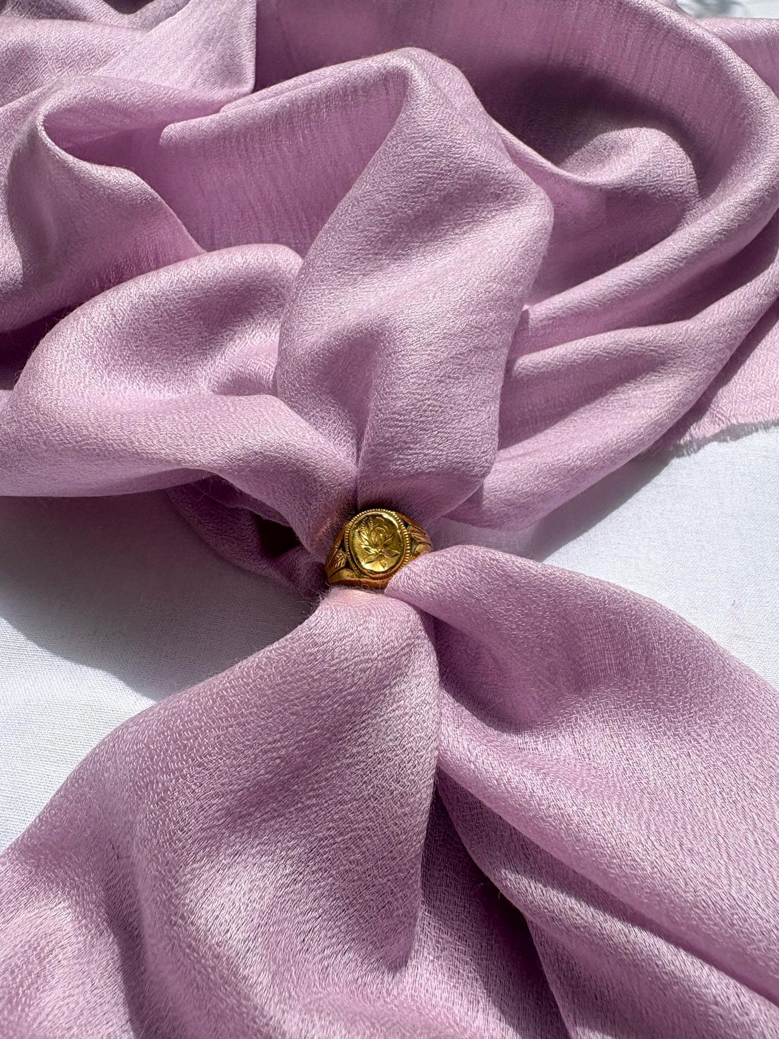 Close-up of a pink fabric bow with a gold button in the center on a white background