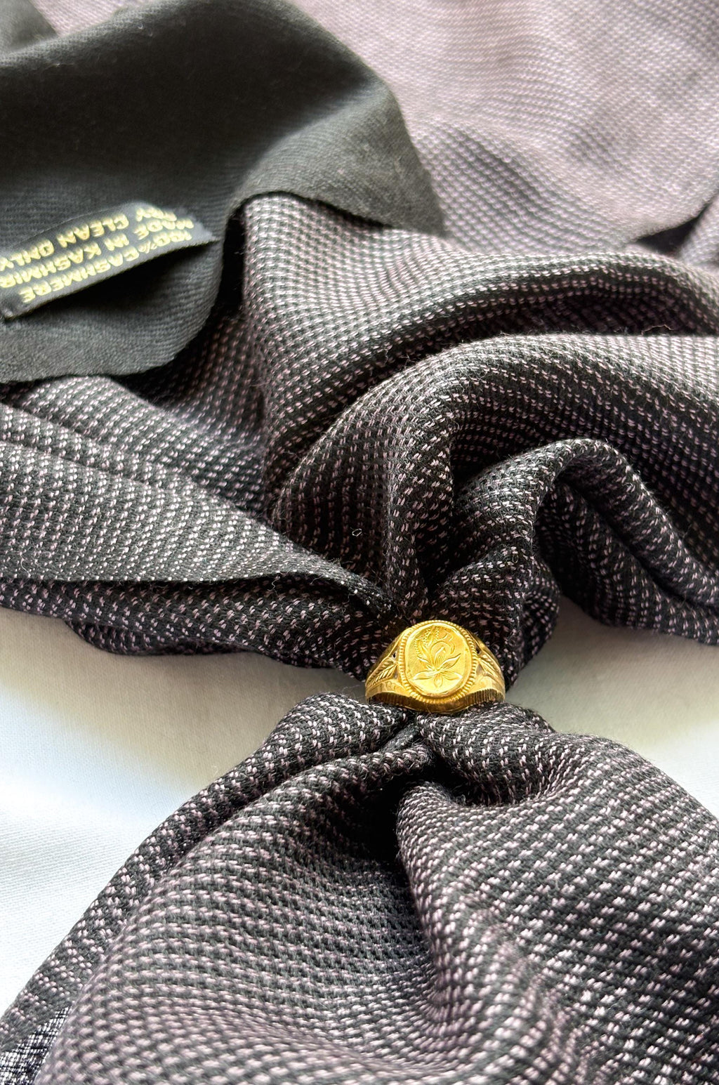 Close-up of a gray textured fabric with a gold ring tied into a knot.