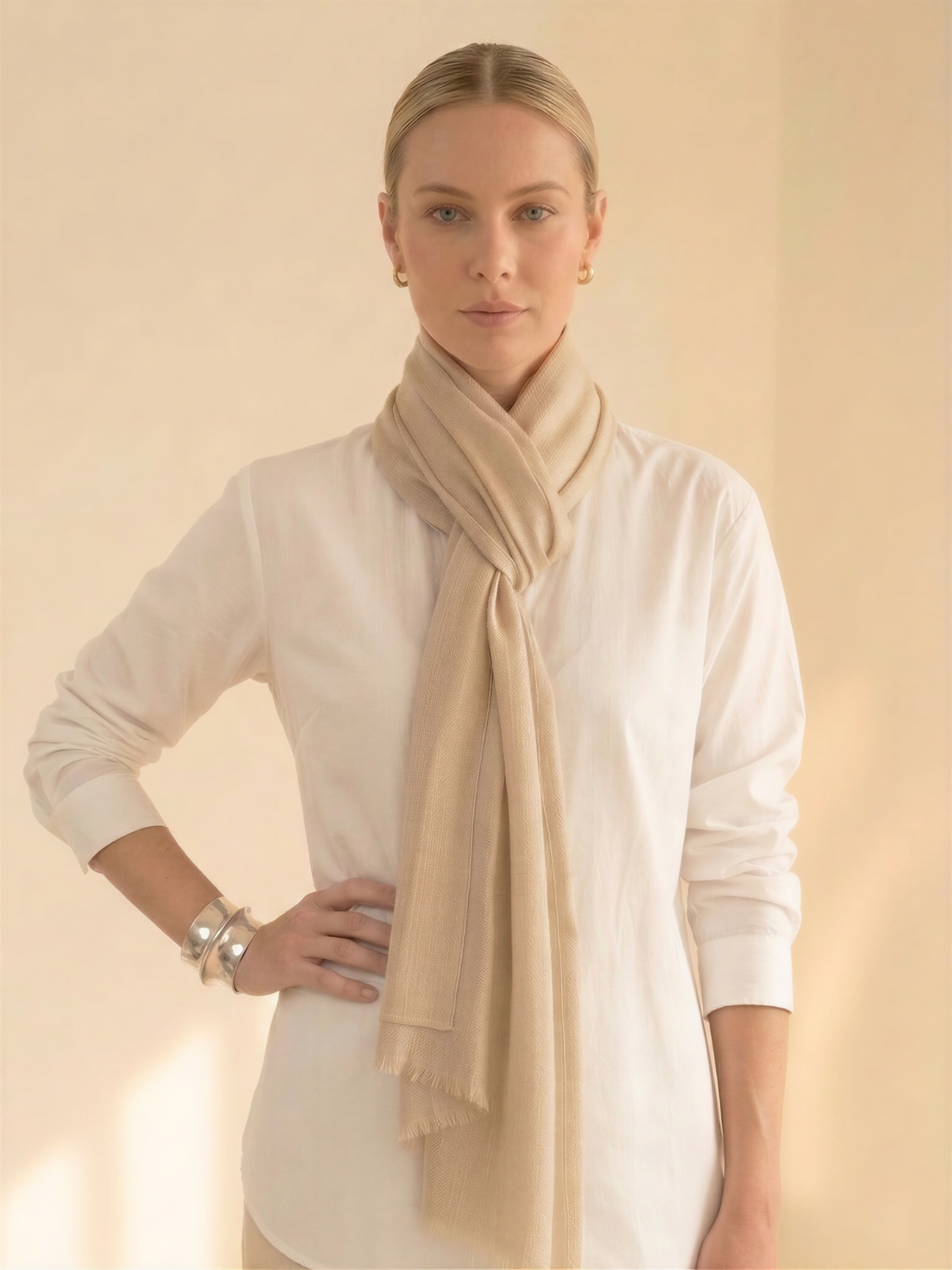 Woman wearing a beige scarf and white shirt against a beige background