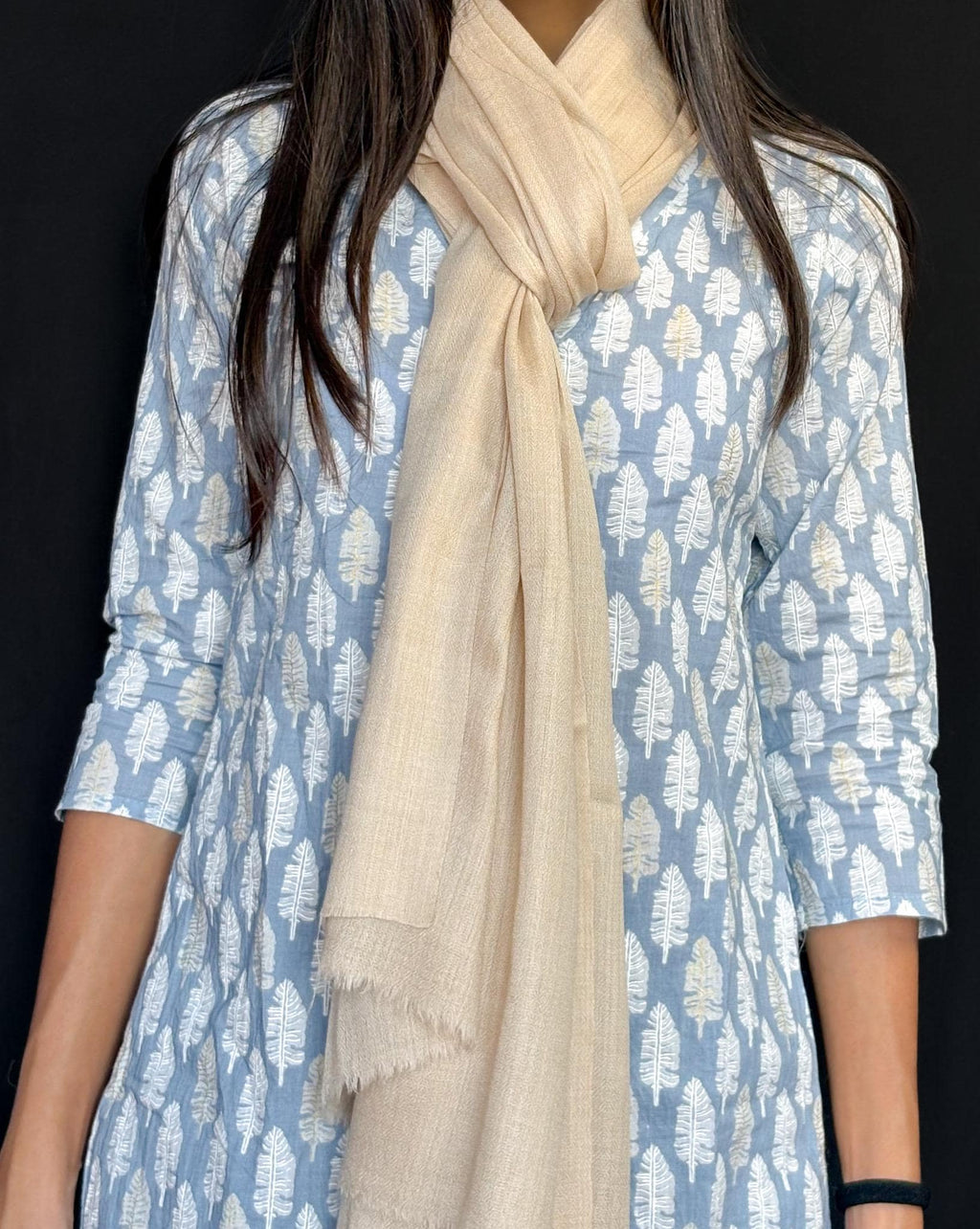 Person wearing a blue patterned dress with a beige scarf against a black background