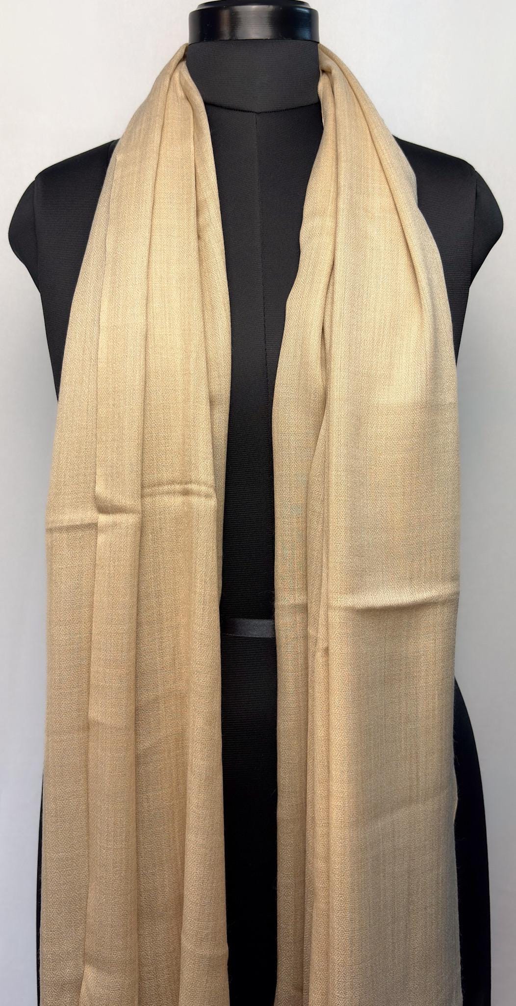 Beige scarf draped over a black mannequin on a white background