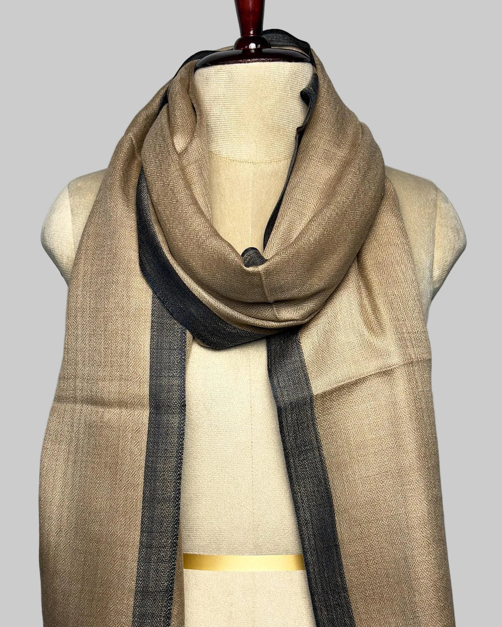 Beige scarf with black accents draped over a mannequin on a plain background