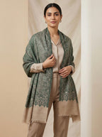 Woman wearing a green patterned shawl over a beige outfit against a beige background