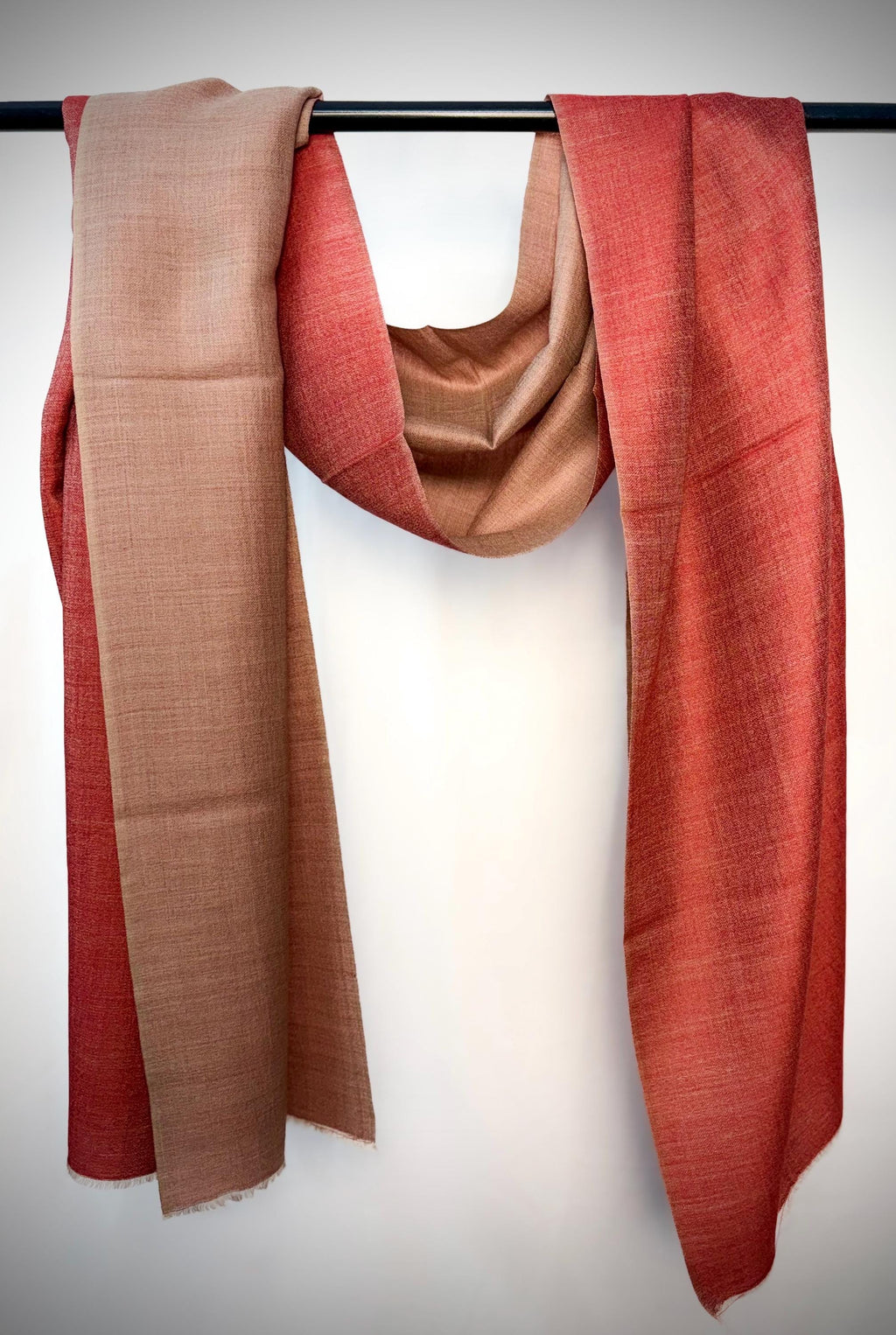 Two scarves in red and brown hanging on a rod against a white background