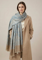 Woman wearing a beige coat and blue patterned scarf against a beige background