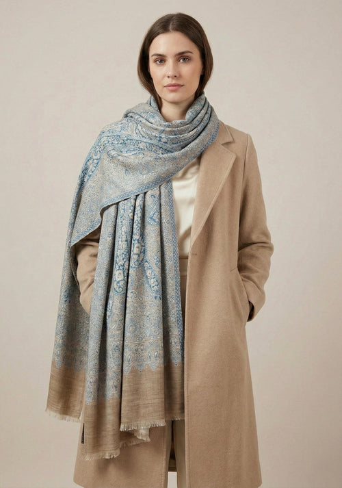 Woman wearing a beige coat and blue patterned scarf against a beige background